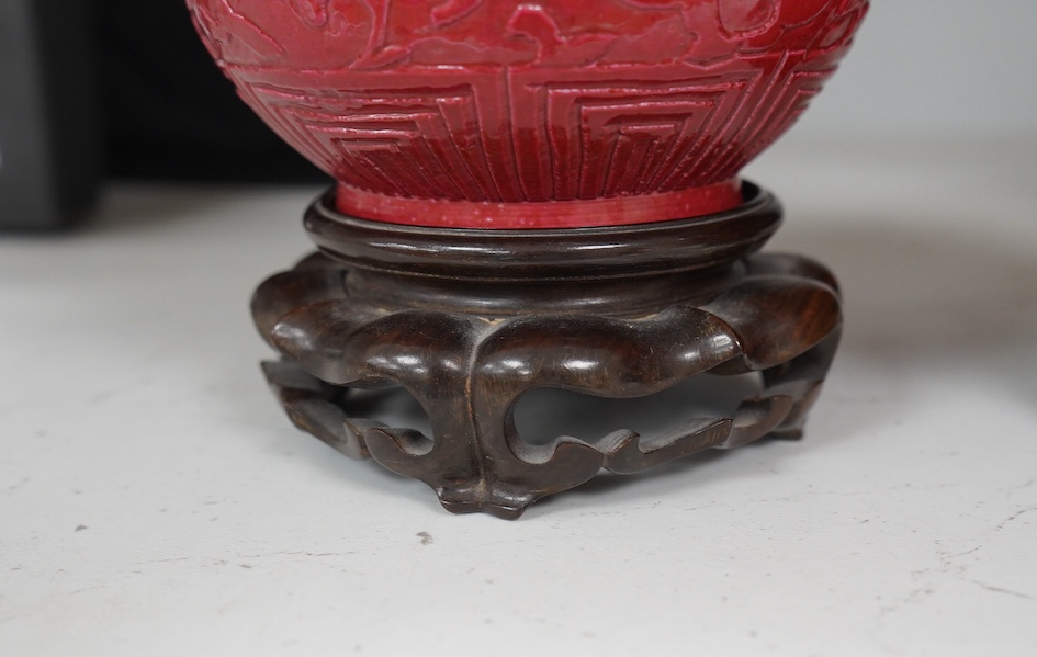 A pair of Chinese ruby ground ‘lotus’ bottle vases, late 19th century, each carved in relief with lotus flowers, scrolling tendrils and leaves, both with carved stands, 24cm high. Condition - one vase the neck broken bot